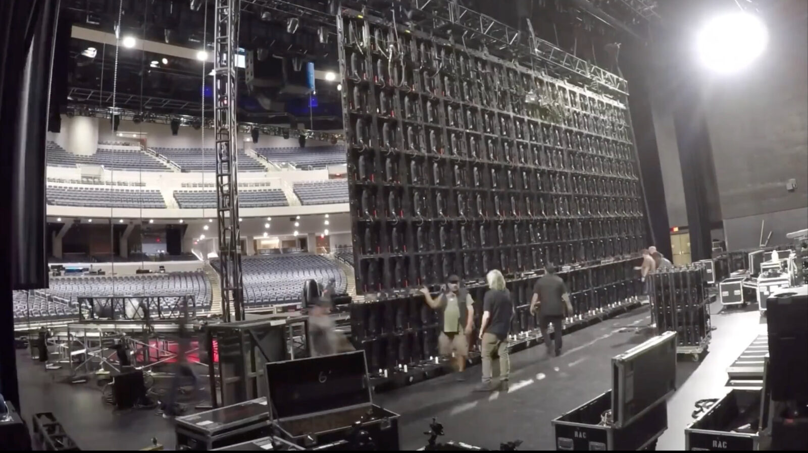 Crew rigging a multi-panel LED video wall from overhead truss inside an arena before doors.